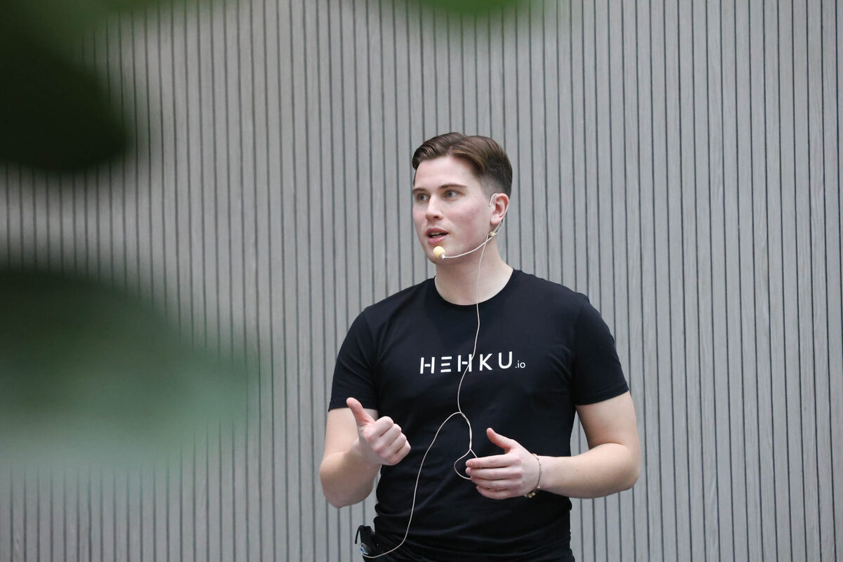 Hehkun puhuja esiintyy tapahtumassa headset-mikrofonin kanssa, yllään musta Hehku-paita.